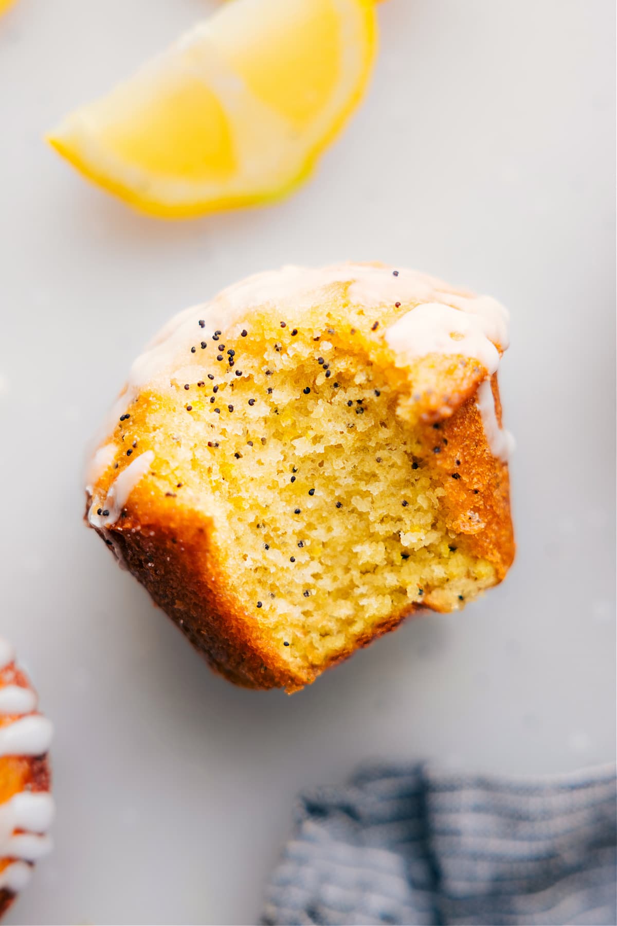 Close-up of a lemon poppy seed muffin with a fresh bite mark, revealing its moist interior, and adorned with creamy frosting.