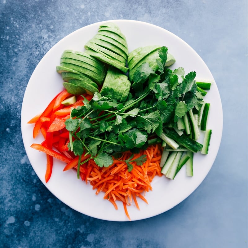 Overhead view of the fresh add-ins for Tuna Salad Wraps: red bell pepper, carrot, cucumber, cilantro and avocado.