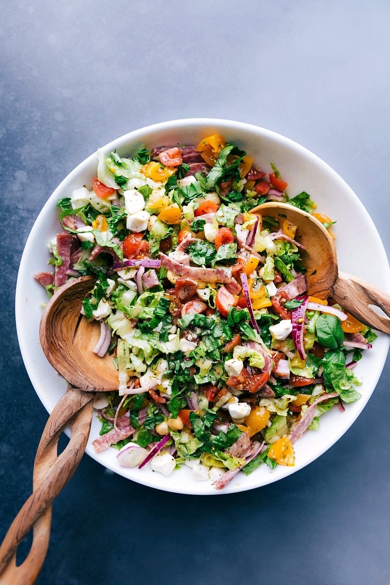 Colorful and vibrant italian chopped salad with wooden serving spoons in the bowl.