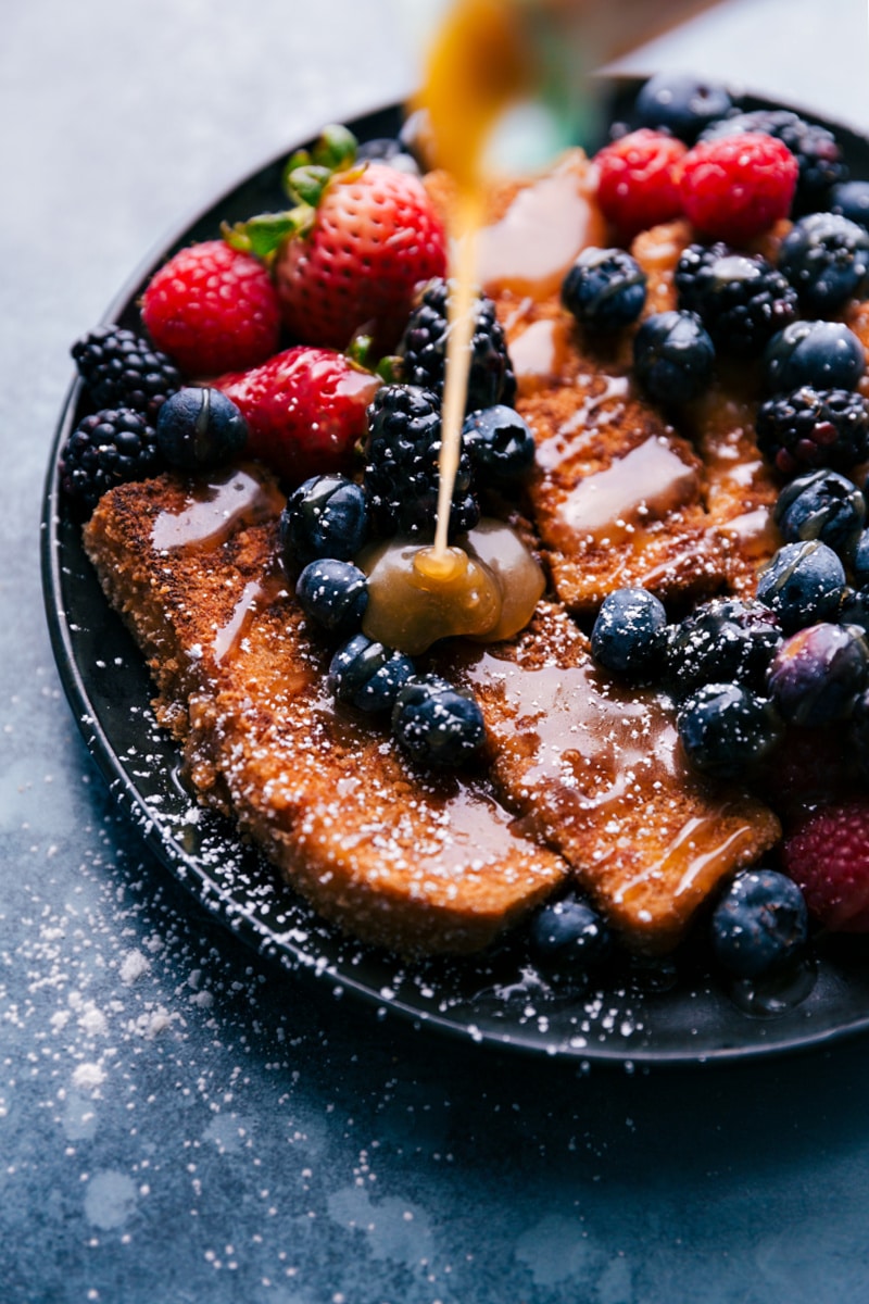 The breakfast on a plate with maple syrup and fresh berries on top.