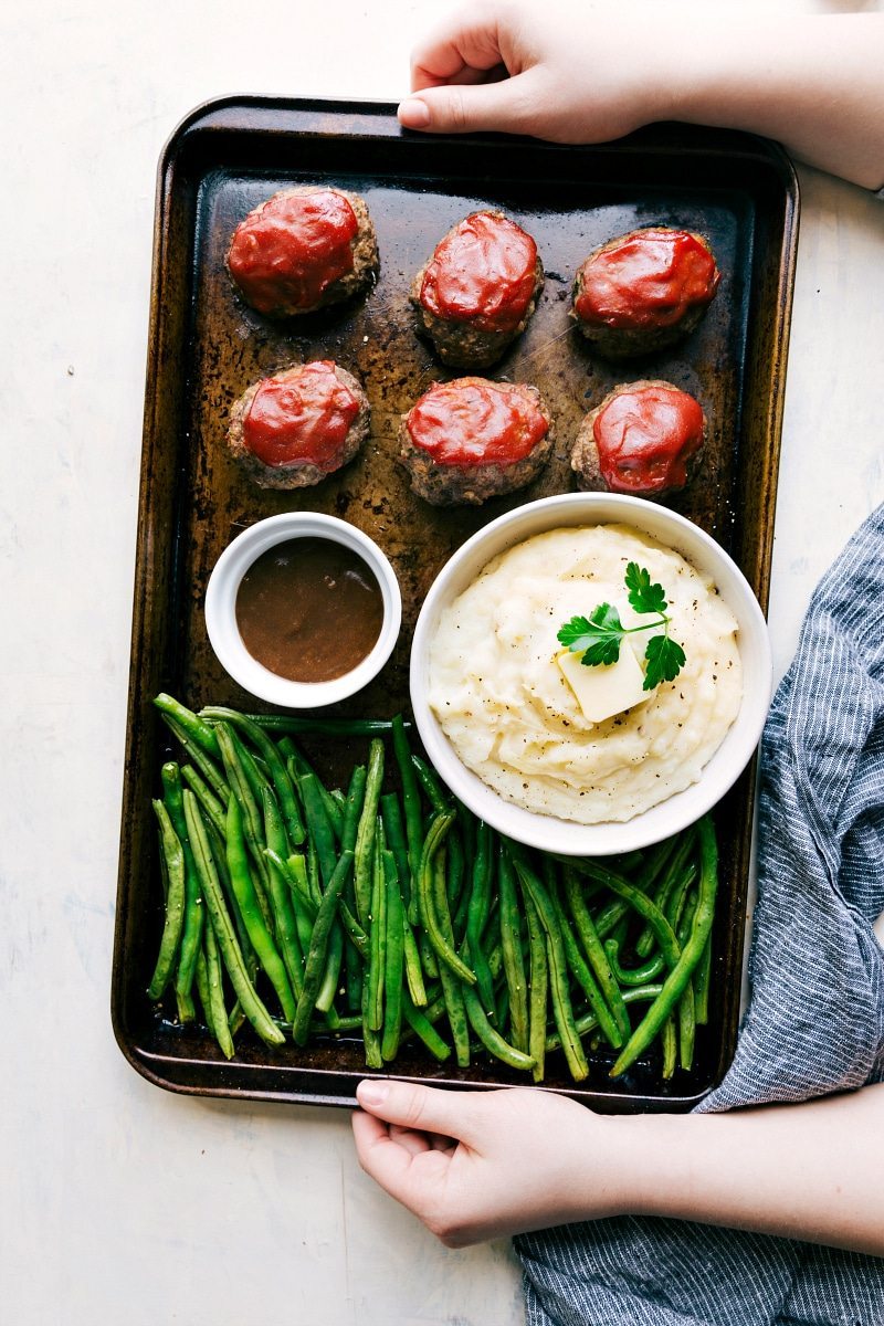 Overhead shot of the mini meatloaves all on one pan with potatoes, green beans, and gravy 