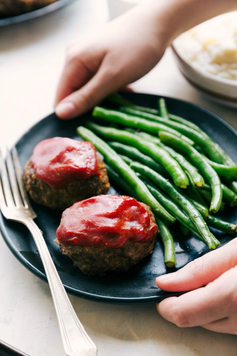 image of two mini meatloafs on a plate with green beans and a fork on the side