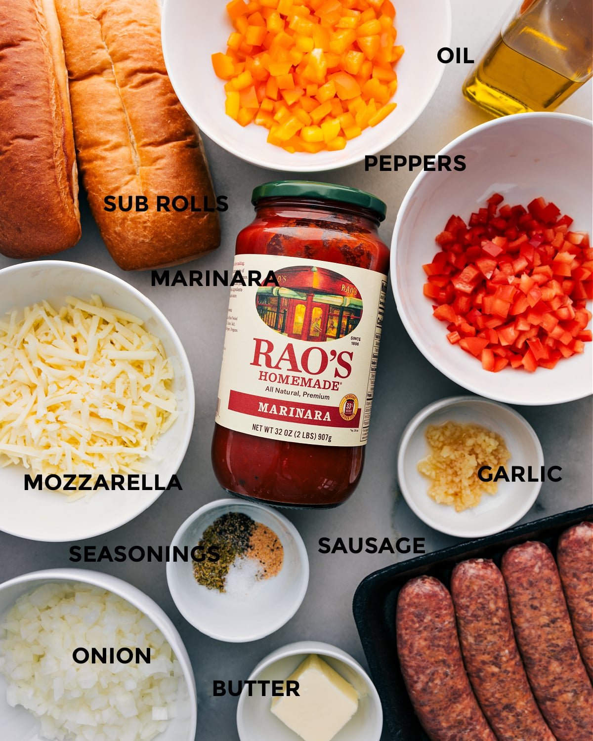 All the ingredients for this recipe are prepped and ready for easy assembly, including peppers, rolls, marinara, mozzarella, onion, seasonings, sausage, garlic, and butter.