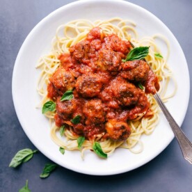 Chicken parmesan meatballs on a bed of pasta in a delicious red sauce, garnished with fresh herbs.