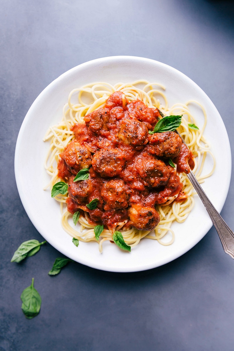 Chicken parmesan meatballs on a bed of pasta in a delicious red sauce, garnished with fresh herbs.