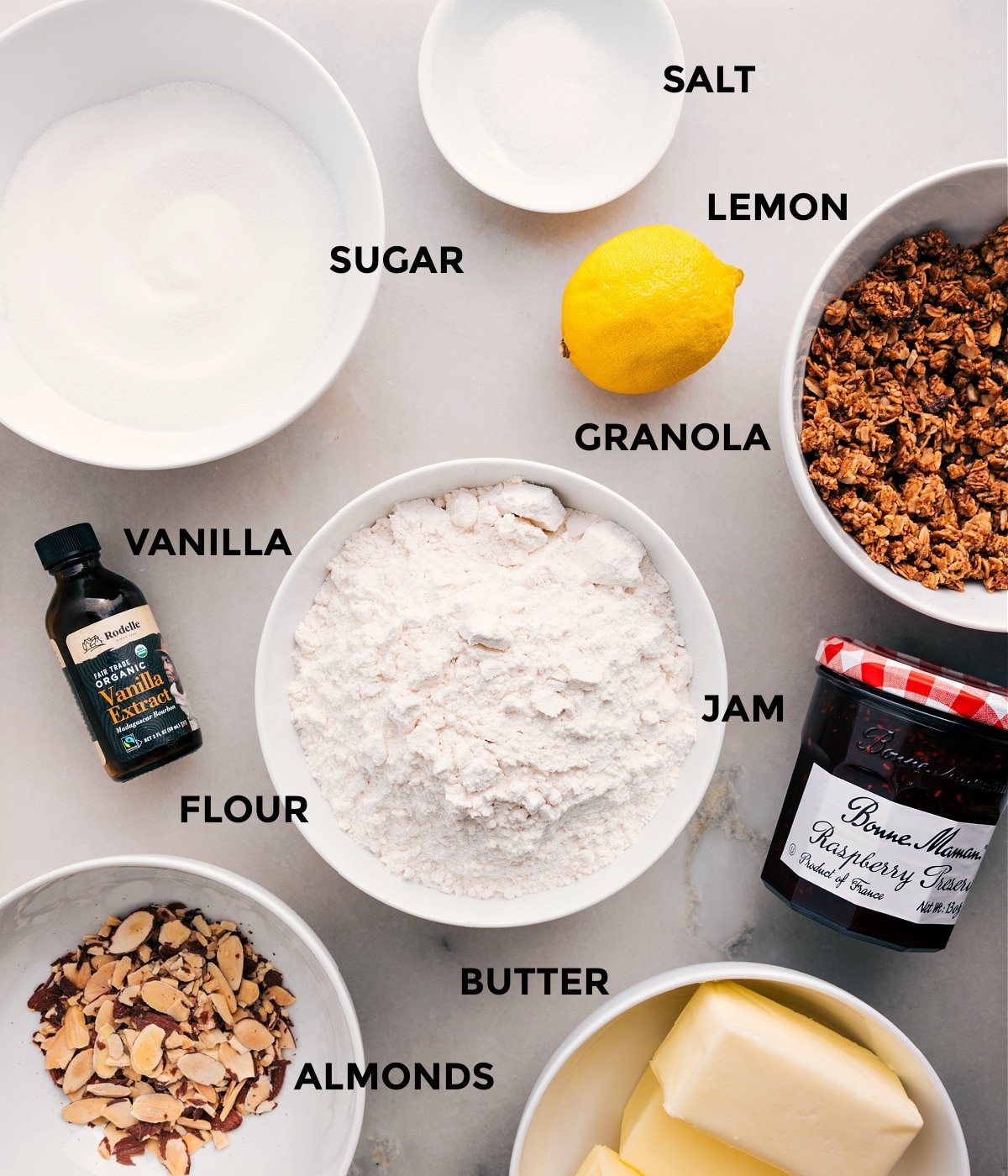 All the ingredients prepped and ready for easy assembly—lemon, granola, jam, flour, vanilla, sugar, salt, butter, and almonds.