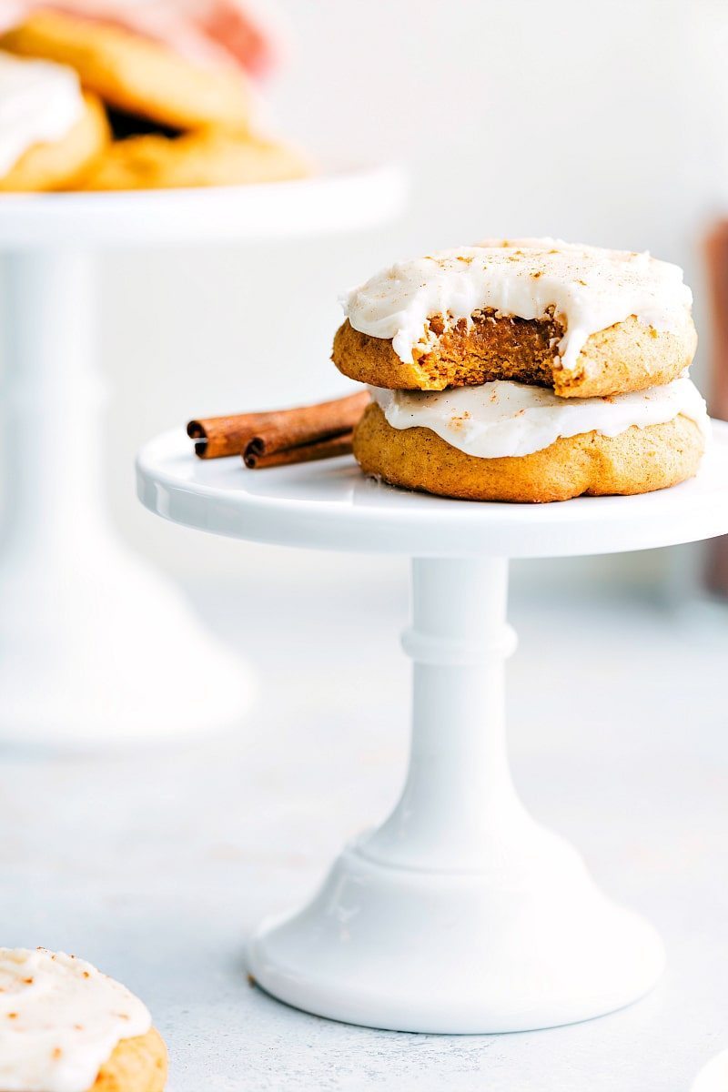 Two soft pumpkin cookies with cream cheese frosting, one with a bite taken out to reveal the fluffy interior.