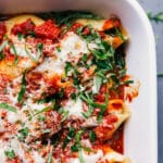 A pan of stuffed shells with sausage, topped with melted cheese and a basil chiffonade, presenting a warm and delicious meal suitable for any occasion.
