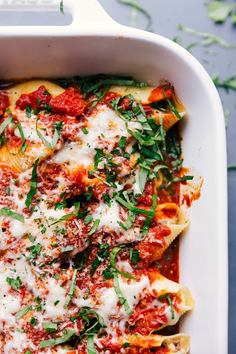 Overhead view of a pan of Stuffed Shells with Sausage, topped with melted cheese and basil chiffonade.