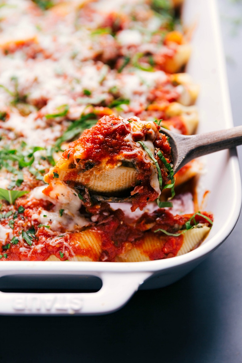 Up-close image of a serving spoon scooping out Stuffed Shells and Sausage.