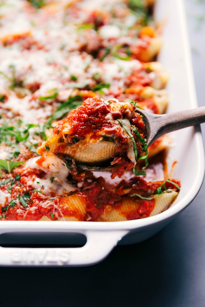 A serving spoon scooping out a hearty portion of savory stuffed shells with italian sausage from a baking dish.