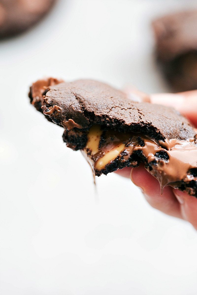 Half of a cookie being held up with caramel oozing out