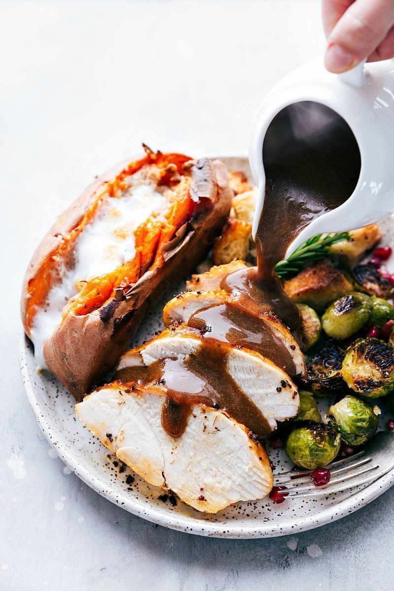 Gravy being poured over a freshly cooked Thanksgiving dinner plate, featuring a meal prepared on two sheet pans.