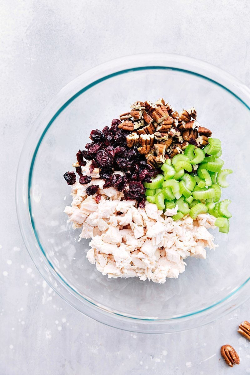 Ingredients for this recipe including chunks of chicken, walnuts, chopped celery, and cranberries in a mixing bowl.