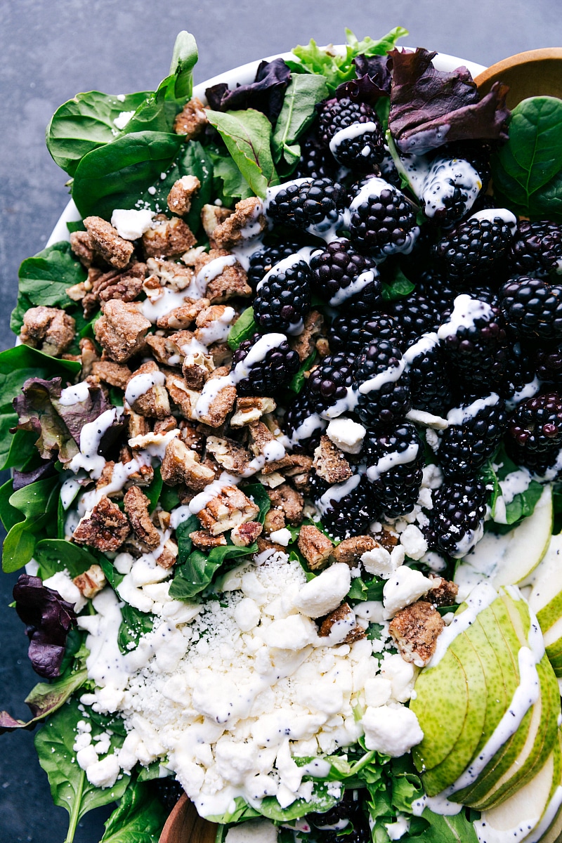 Blackberry salad featuring a drizzle of poppy seed dressing over a mix of blackberries, nuts, greens, and cheese.