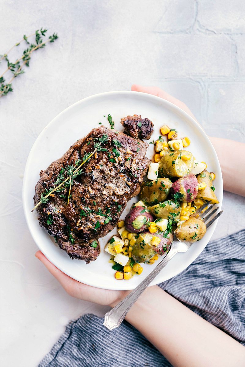 Two hands holding a plate with skillet steak and potato salad