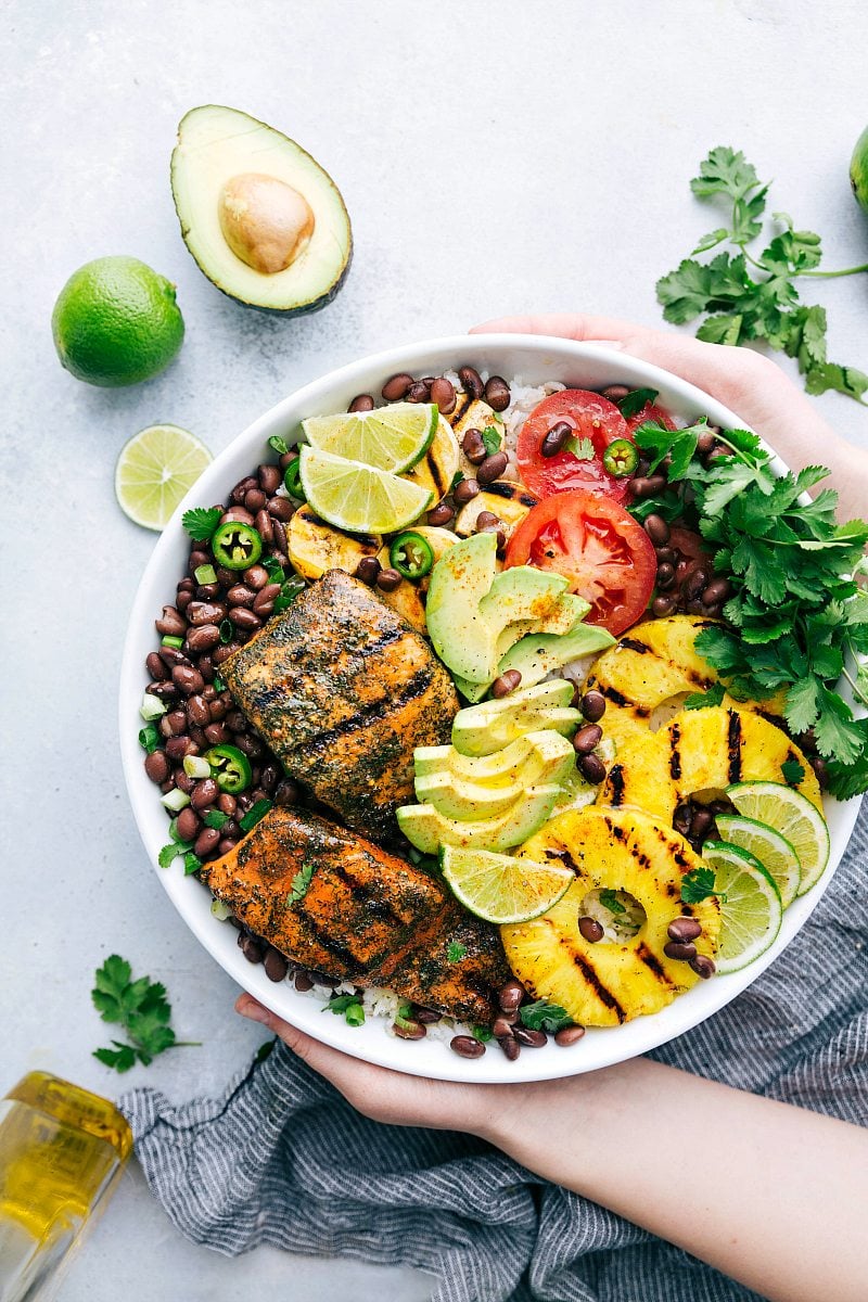 Two hands holding a bowl of mojo salmon bowls