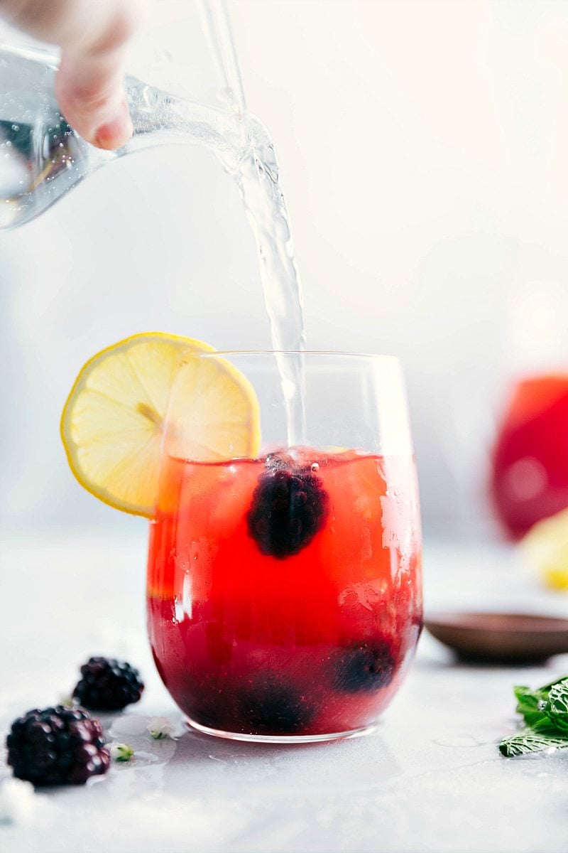 Sparkling water being poured into a glass of Blackberry Lemonade.