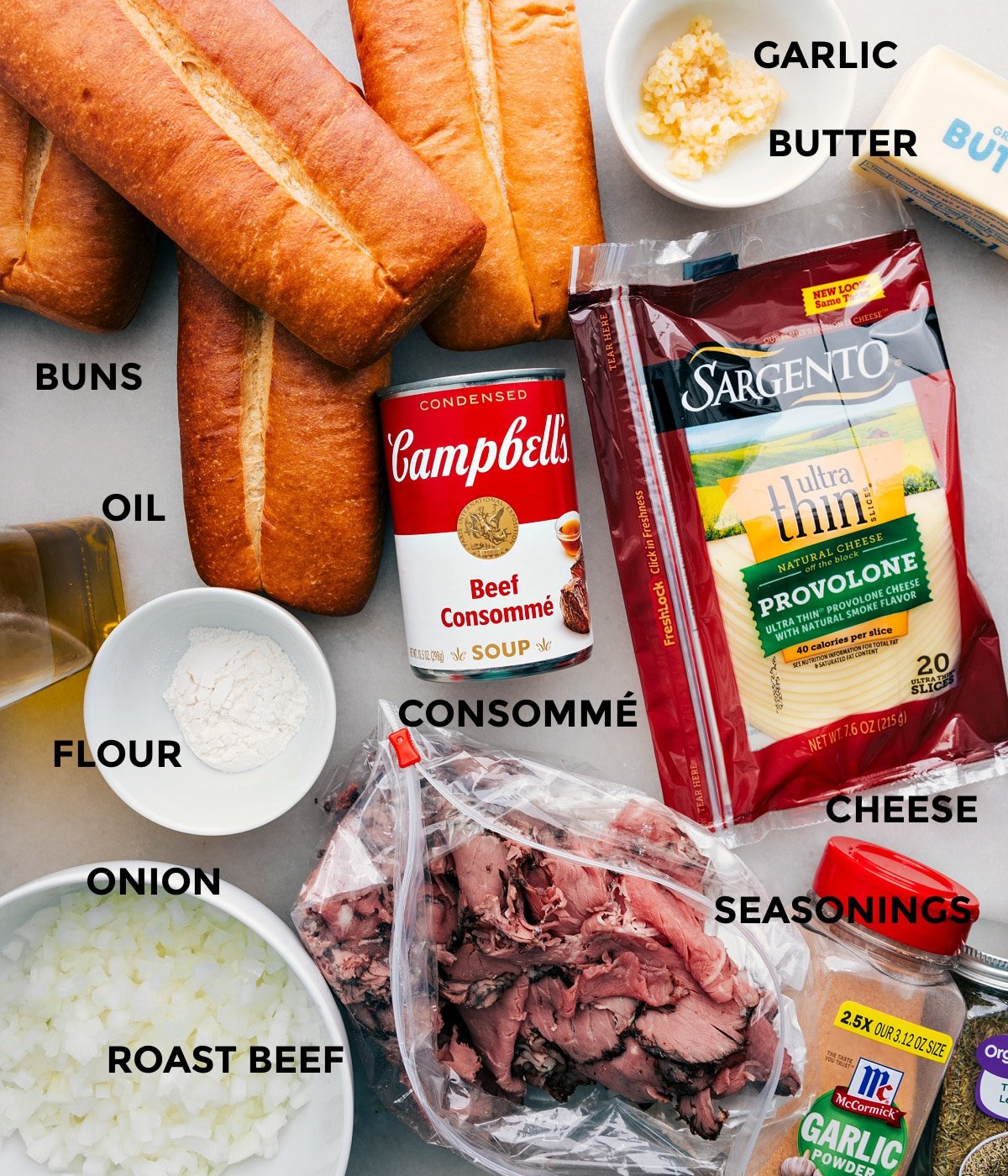 All the ingredients including buns, oil, flour, onions, roast beef, garlic, butter, cheese, seasonings, and consomme prepped out for easy assembly.