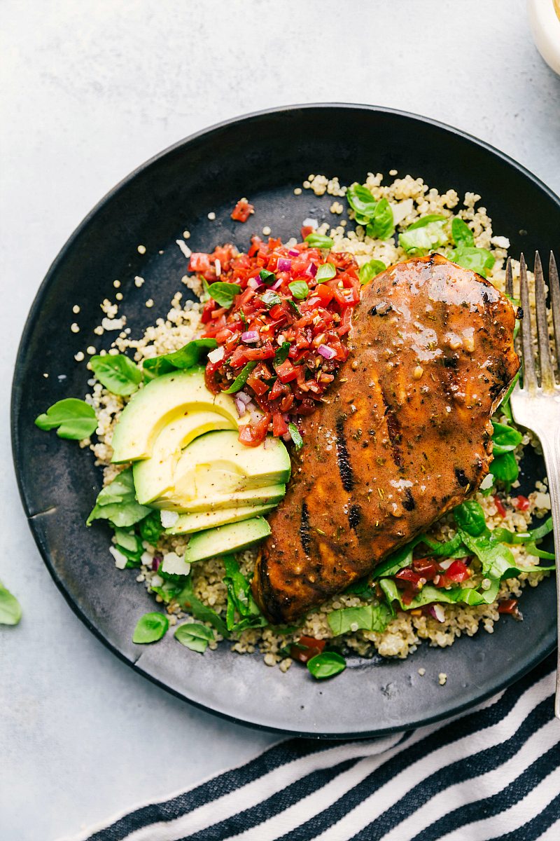 Plate of bruschetta chicken served over quinoa with bruschetta tomato topping and fresh avocado