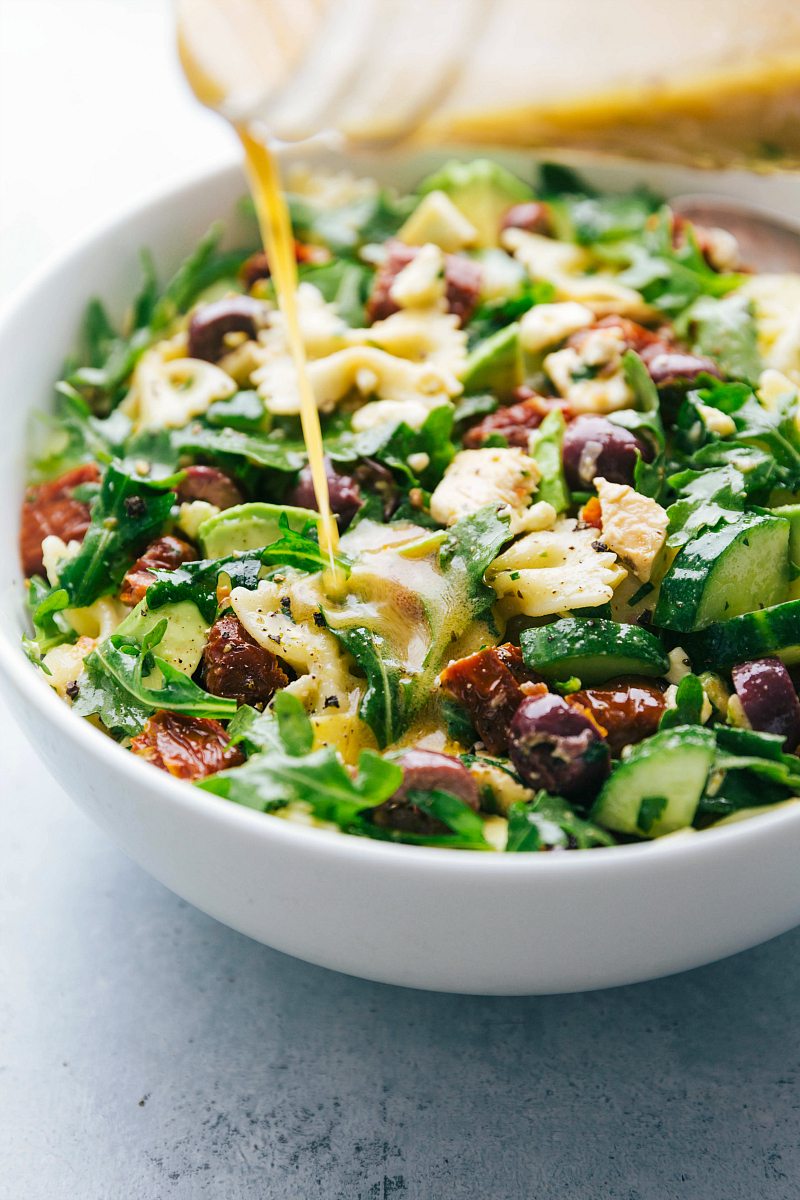 Chicken pasta salad with dressing being poured over it. The salad is in a white bowl. 