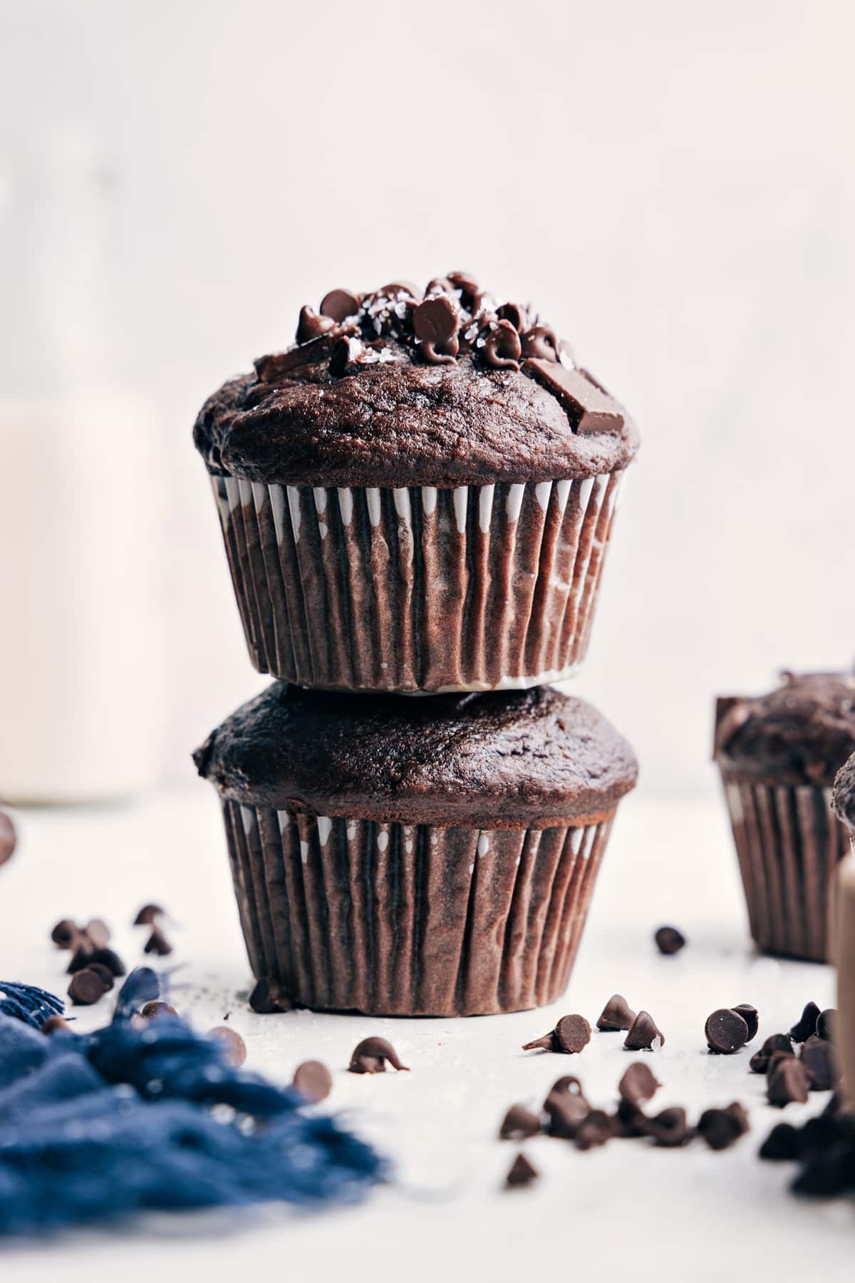 Decadent And Delicious Chocolate Banana Muffins Chocolate Banana Muffins stacked on top of each other with chocolate chips and flaky sea salt sprinkled on top.