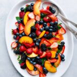 A large platter filled with a vibrant and gorgeous fruit salad, featuring an array of fresh fruits, beautifully arranged, showcasing a rainbow of colors and textures.