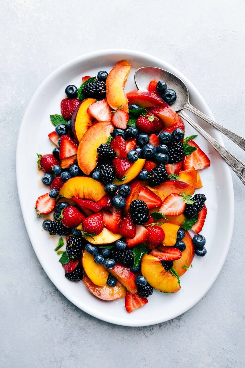 A large platter filled with a vibrant and gorgeous fruit salad, featuring an array of fresh fruits, beautifully arranged, showcasing a rainbow of colors and textures.