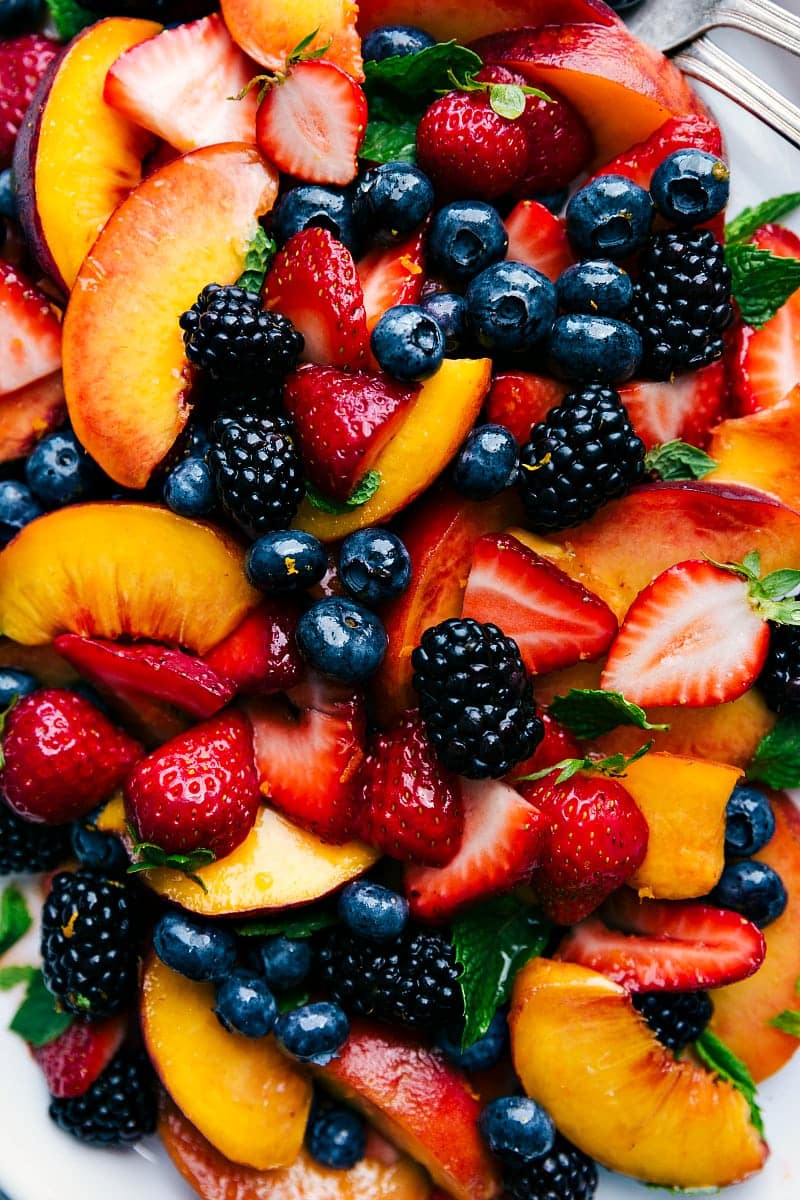 The completed dish from the recipe for fruit salad, showcasing a mix of various fruits including strawberries, blackberries, blueberries, and peaches, with fresh basil scattered throughout, making it an ideal dish for any occasion.