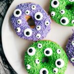 The monster Halloween donuts on a plate covered with purple and green sprinkles and candy eyes.