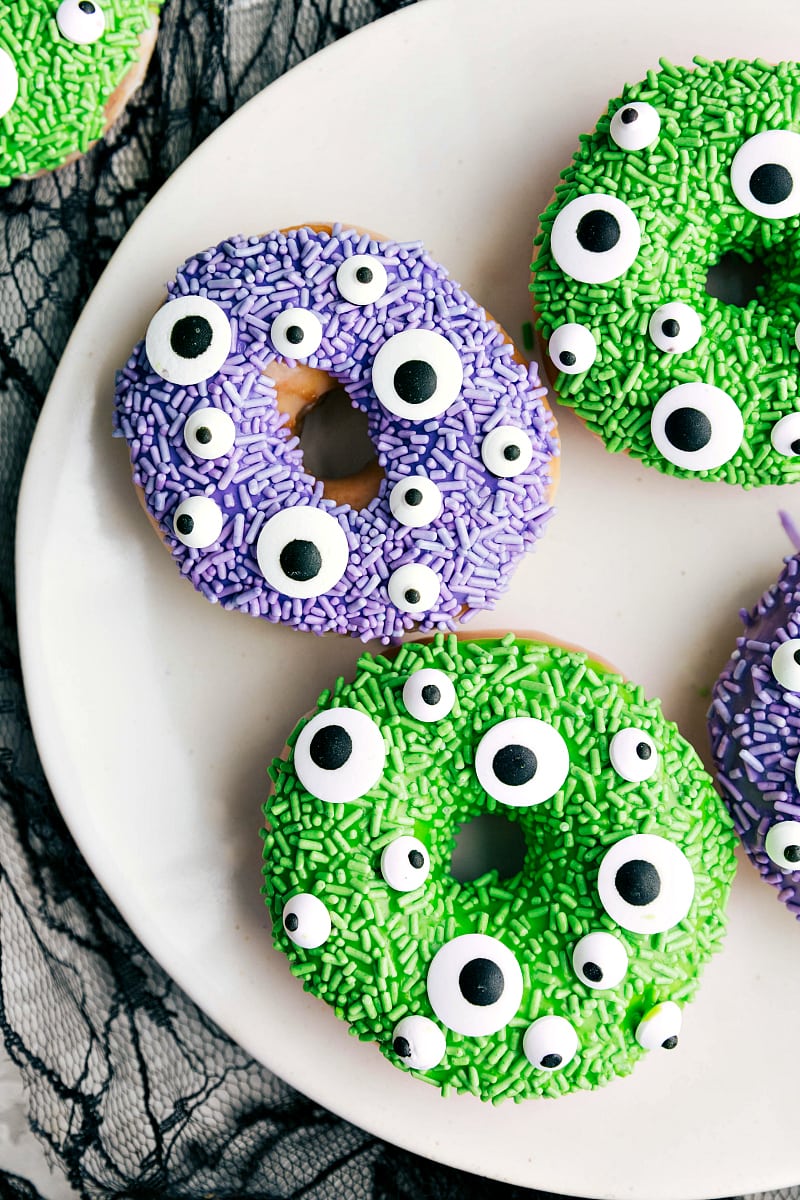 The monster Halloween donuts on a plate covered with purple and green sprinkles and candy eyes.