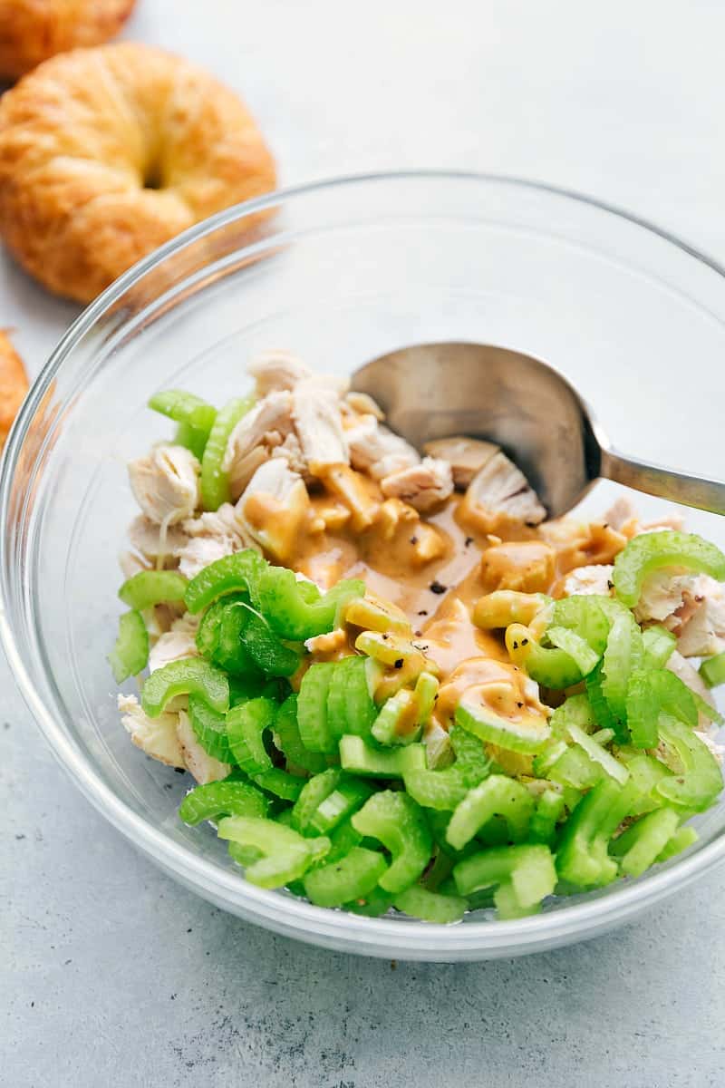 Honey Mustard Chicken Salad Sandwich mixture in a bowl being mixed together with croissant rolls in the background.