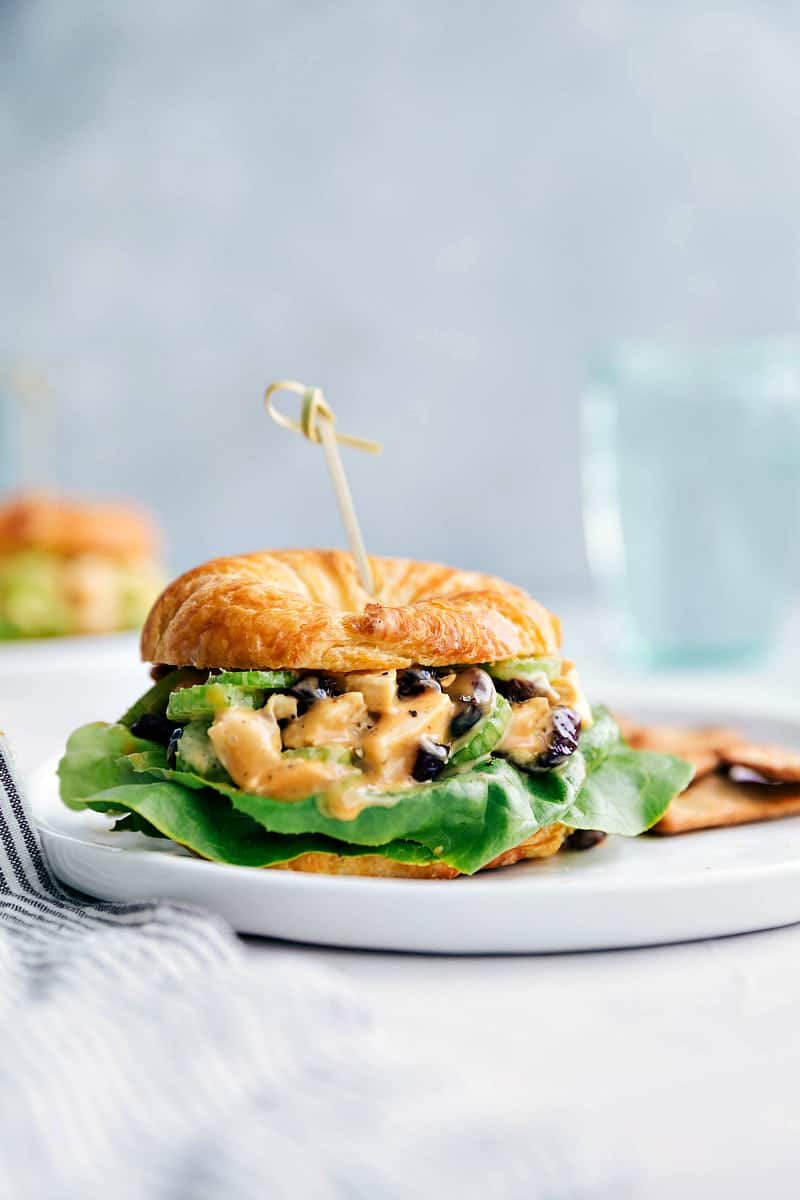 Close-up shot of a Honey Mustard Chicken Salad Sandwich with crackers on the plate and water in the background.