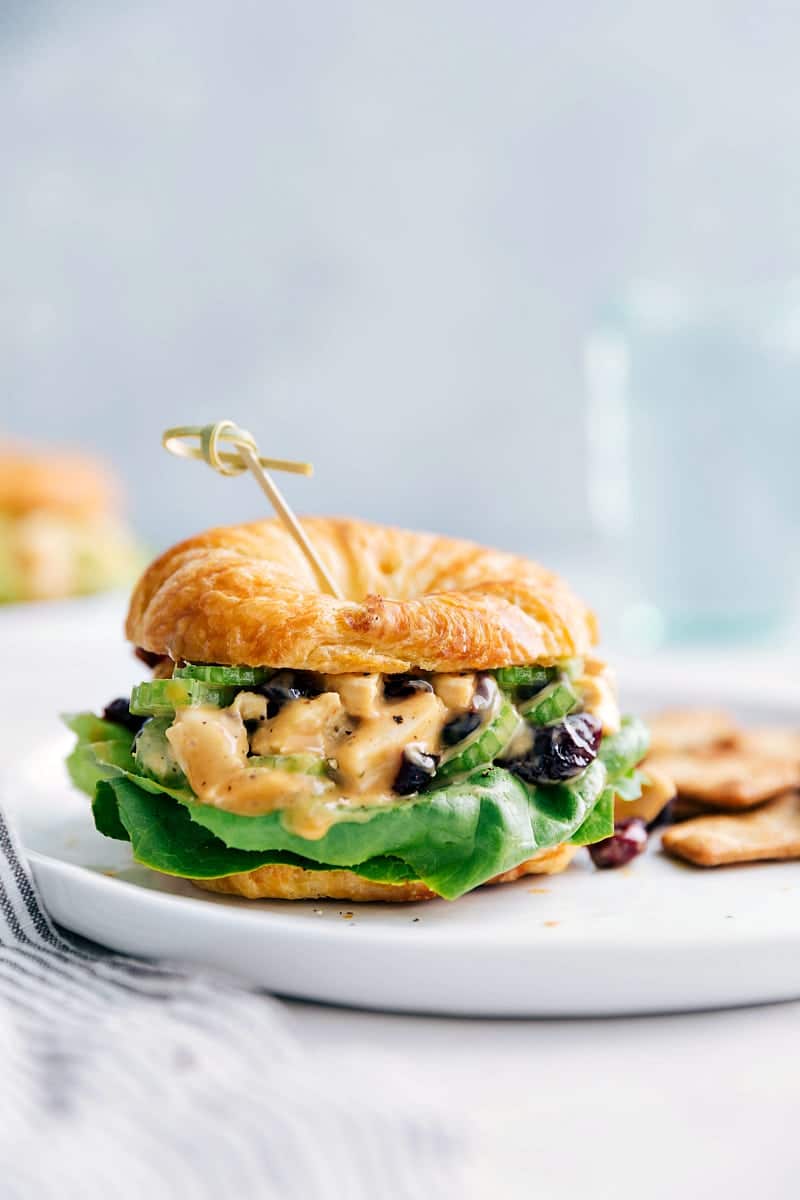 Close-up view of a Honey Mustard Chicken Salad Sandwich with crackers on the plate and water in the background.