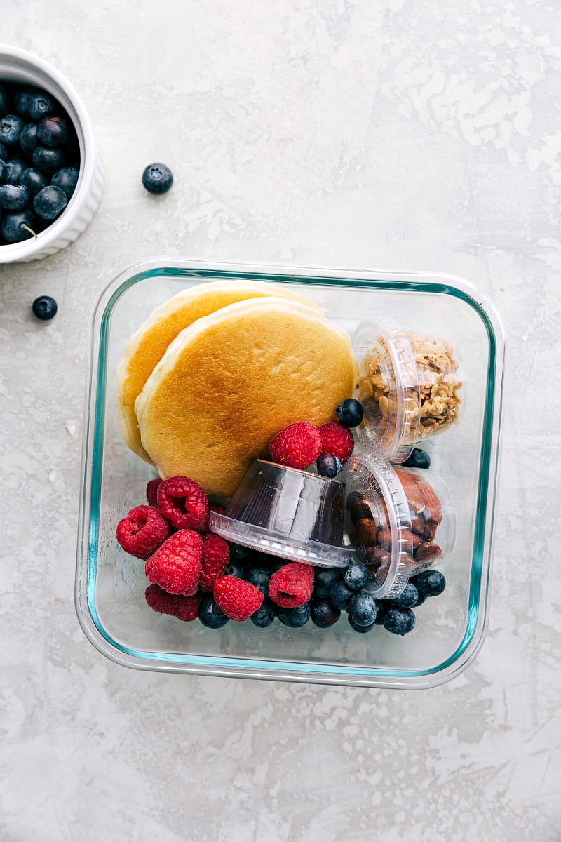 View of the pancakes, suryp, granola, nuts and fruit, all packed and ready to go to school for lunch.