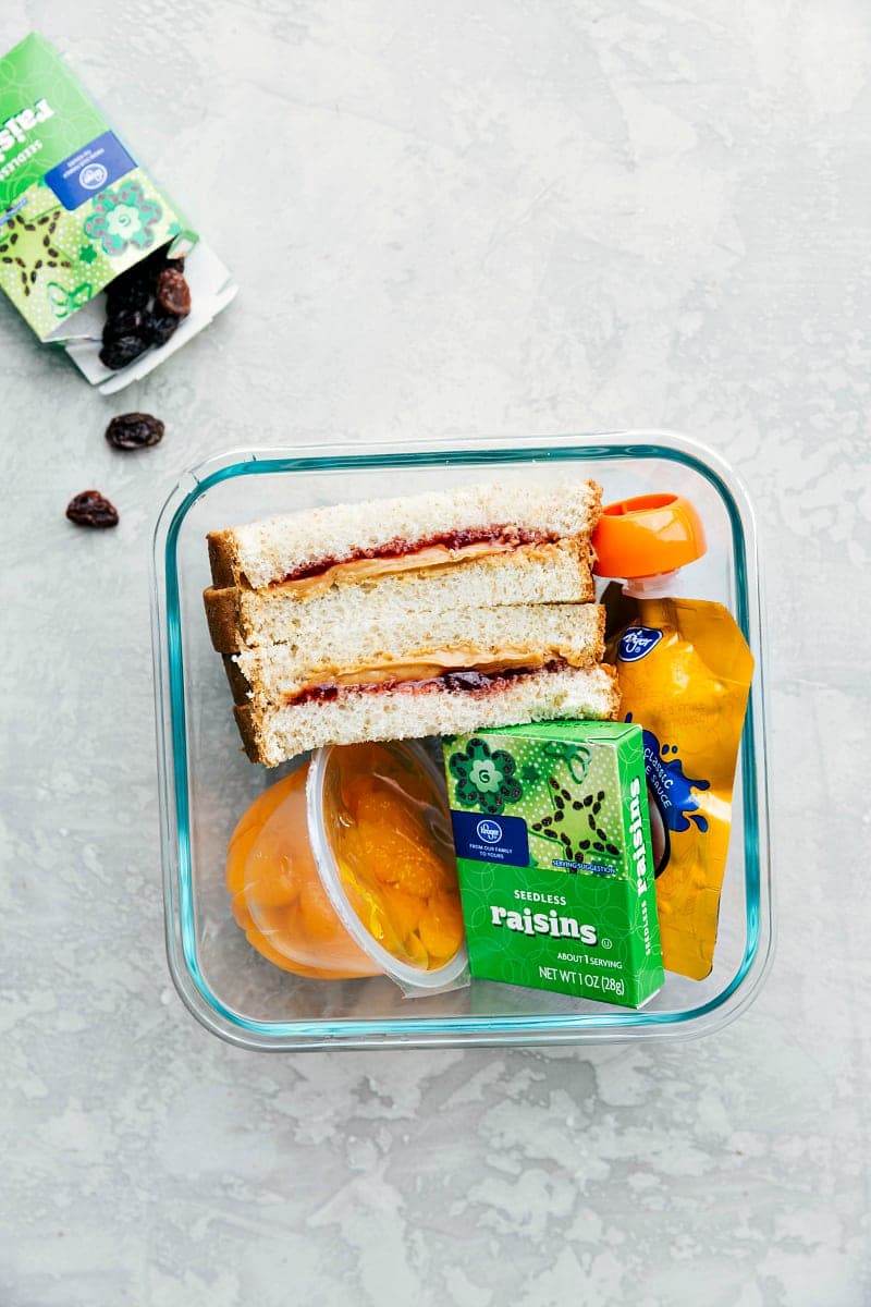 Overhead view of a school lunch: PBJ, raisins and Mandarin oranges.