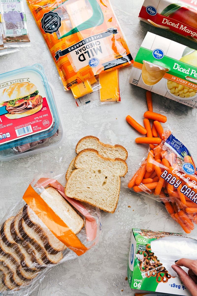 View of the components in another good school lunch: sliced deli meat, cheese, fruit, bread, veggies and a fruit snack.