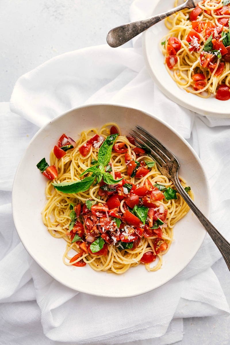 Overhead shot of two bowls filled with bruschetta pasta -- parmesan garlic pasta topped with a tomato bruschetta topping