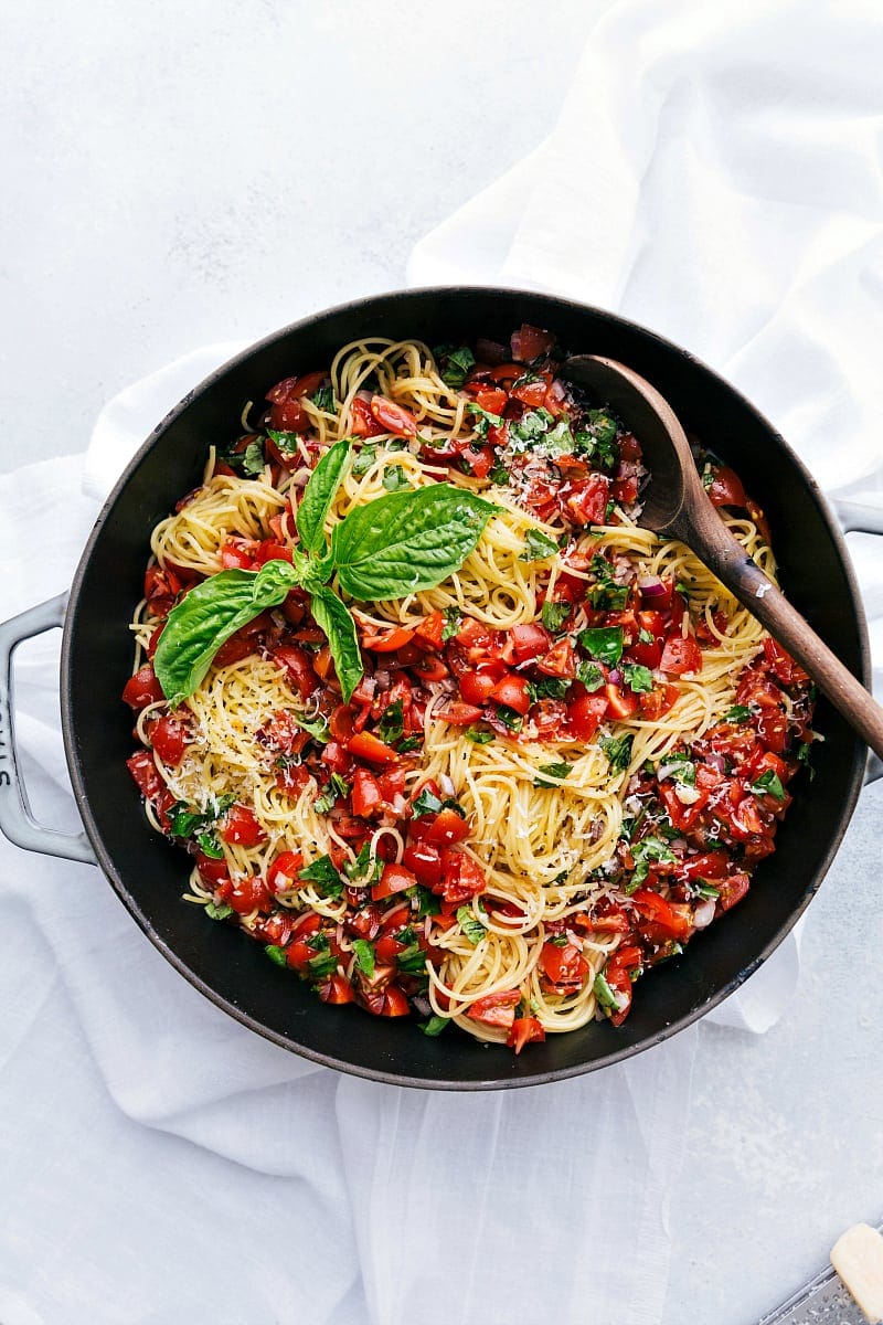 Overhead shot of large pot filled with bruschetta pasta -- parmesan garlic pasta topped with a tomato bruschetta topping