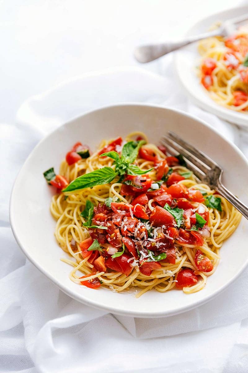 90 degree angle shot of large white bowl filled with bruschetta pasta -- parmesan garlic pasta topped with a tomato bruschetta topping