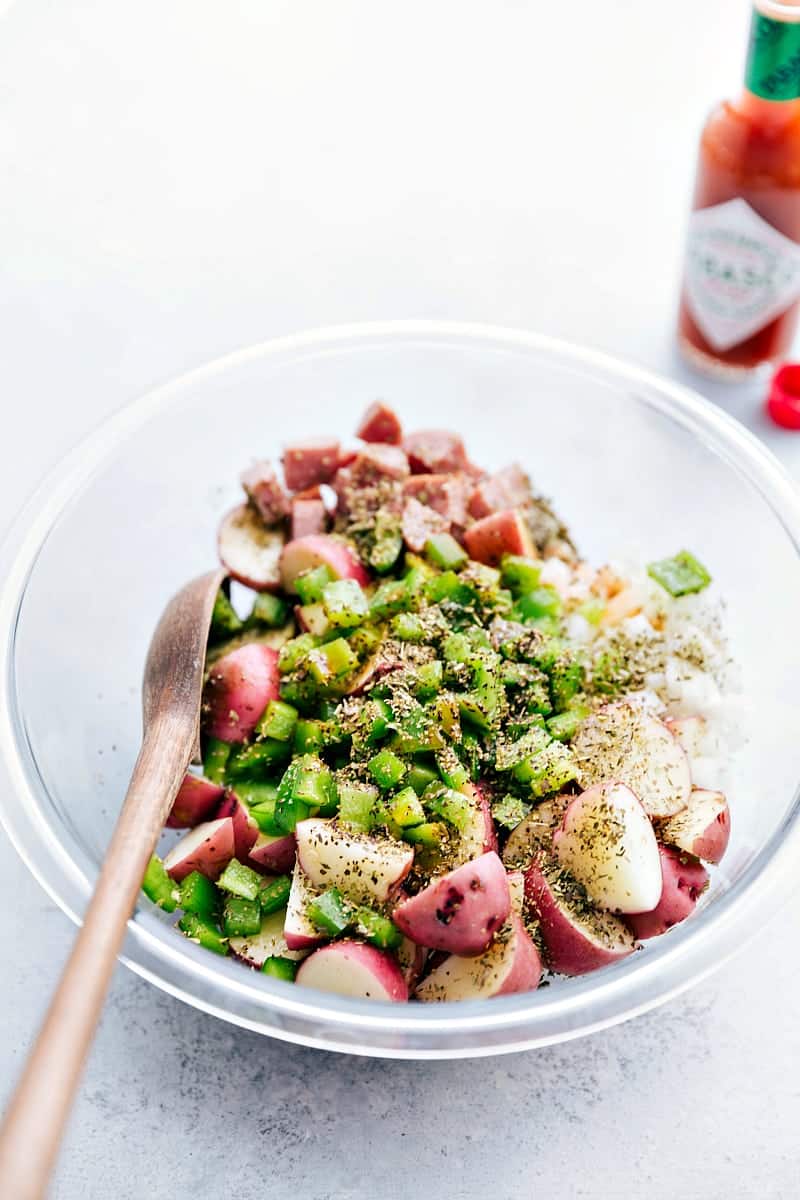 All the veggies, sausages, and seasonings added to a bowl to toss together.