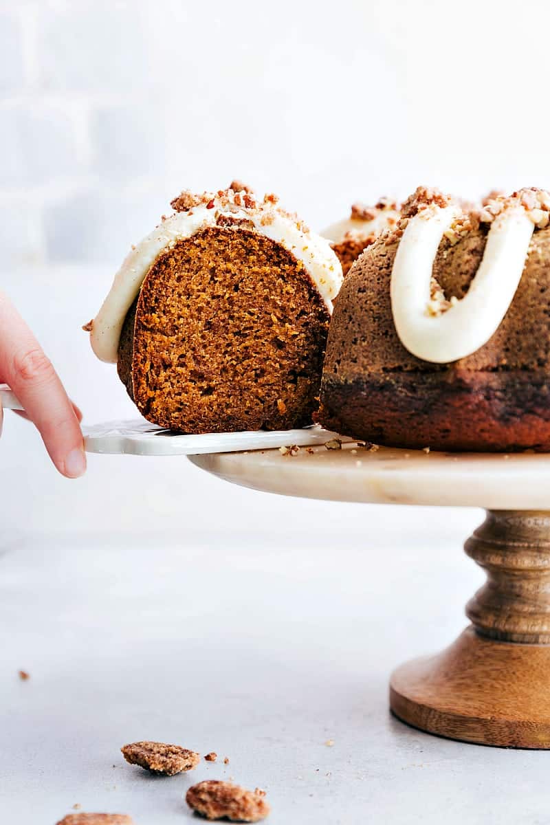 A hand removing a slice of the delicious pumpkin cake from the cake stand.