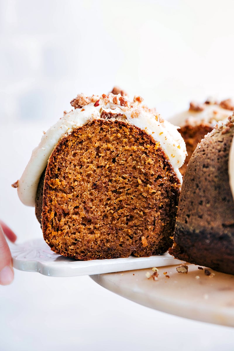 One slice of pumpkin cake with cream cheese frosting being pulled off a cake stand, revealing the moist and fluffy interior.