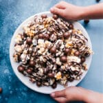 Chocolate Popcorn in a bowl with two hands holding it.