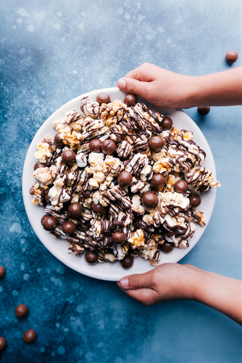 Chocolate Popcorn in a bowl with two hands holding it.