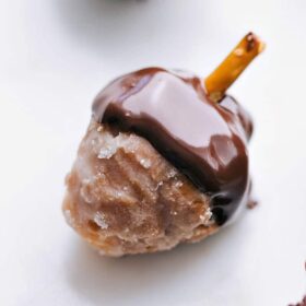 Donut hole with the top dipped in chocolate and a pretzel coming out, resembling an acorn.