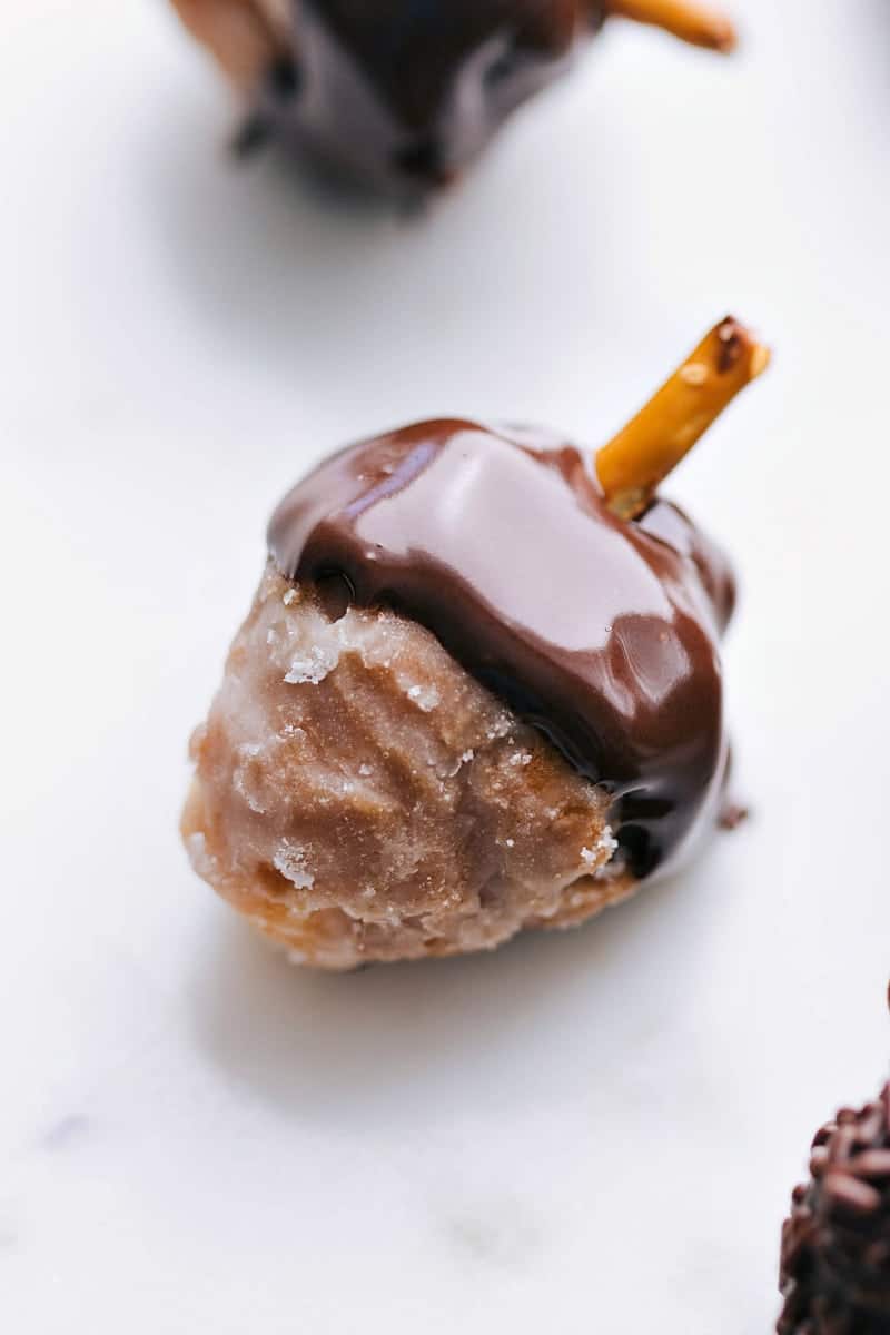 Donut hole with the top dipped in chocolate and a pretzel coming out, resembling an acorn.