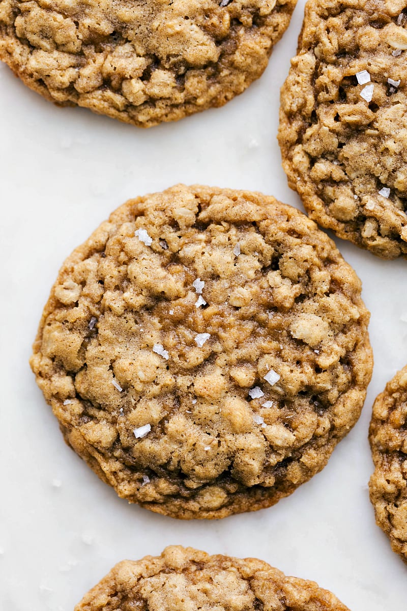 Up close overhead photo of an oatmeal cookie with a sprinkle of sea salt on top and additional oatmeal cookies in the corners of the photo