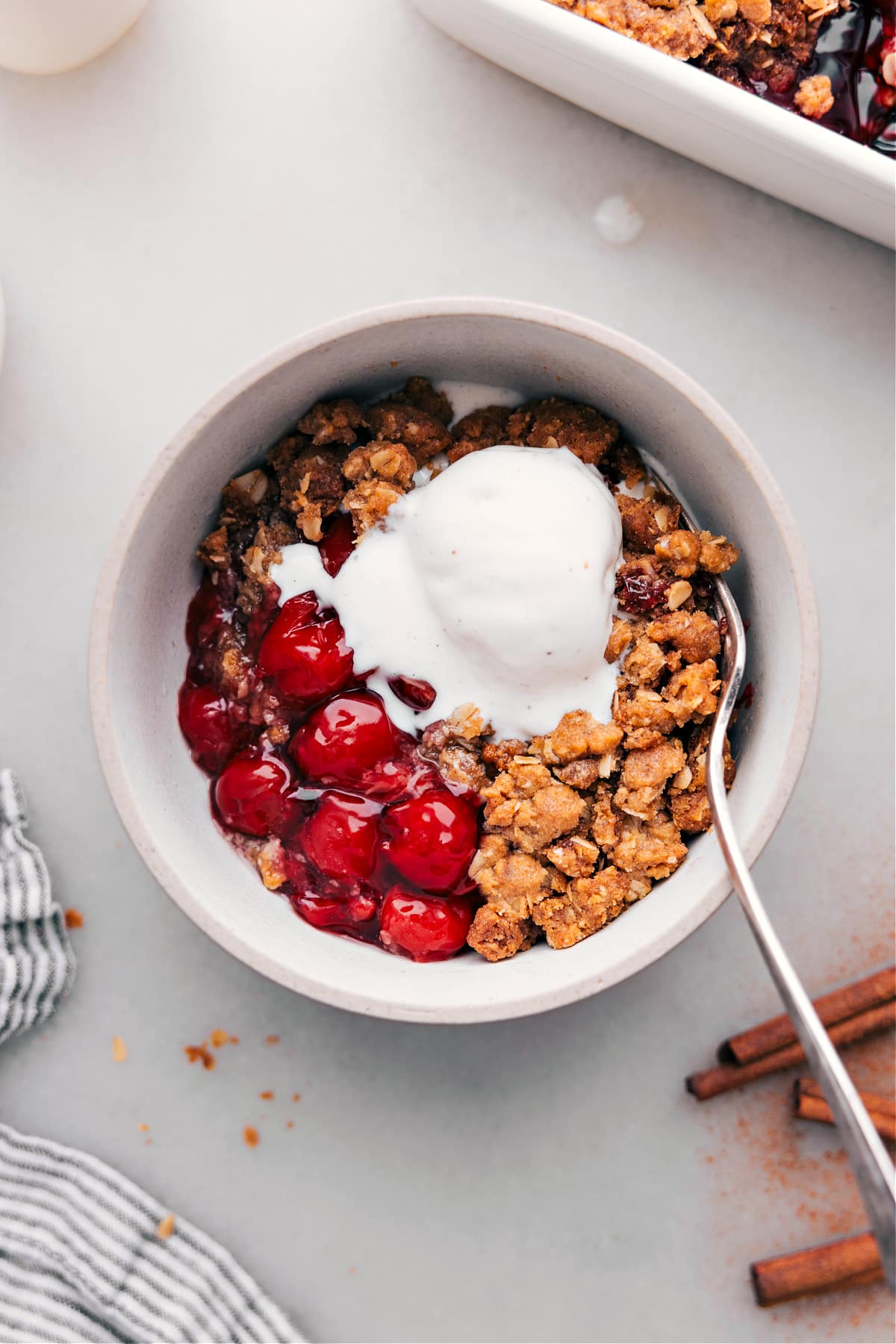 Bowl of fresh cherry crisp recipe crowned with a scoop of creamy vanilla ice cream, a heavenly dessert.