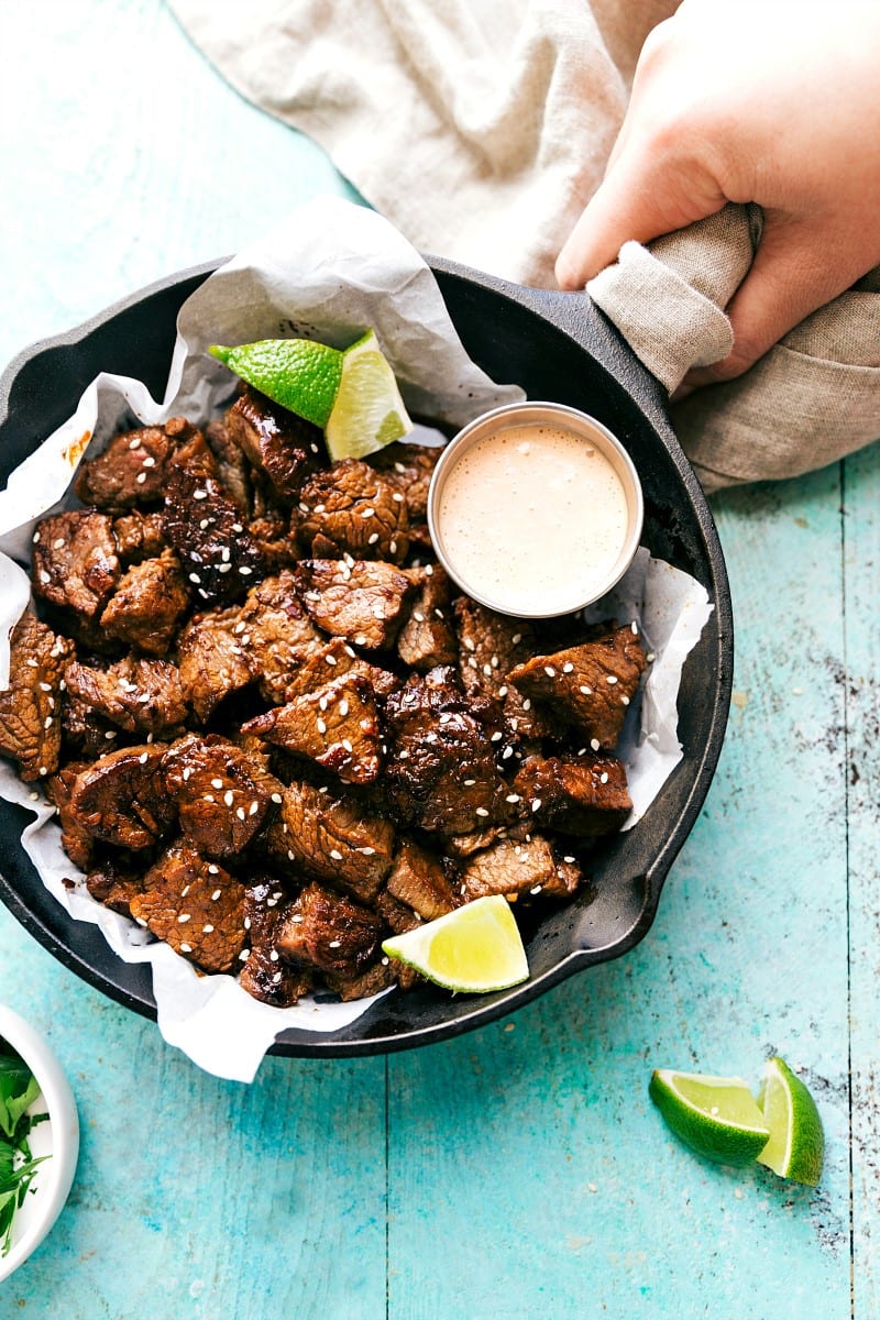 Overhead view of Easy Asian Steak Bites in a skillet along with a small bowl of dipping sauce.